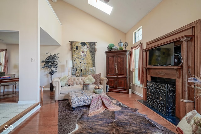 living area with a skylight, a fireplace with flush hearth, wood finished floors, high vaulted ceiling, and baseboards