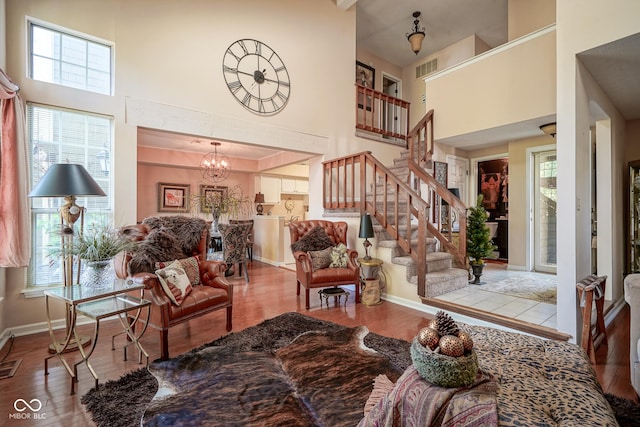 living area featuring stairway, wood finished floors, a towering ceiling, and a notable chandelier