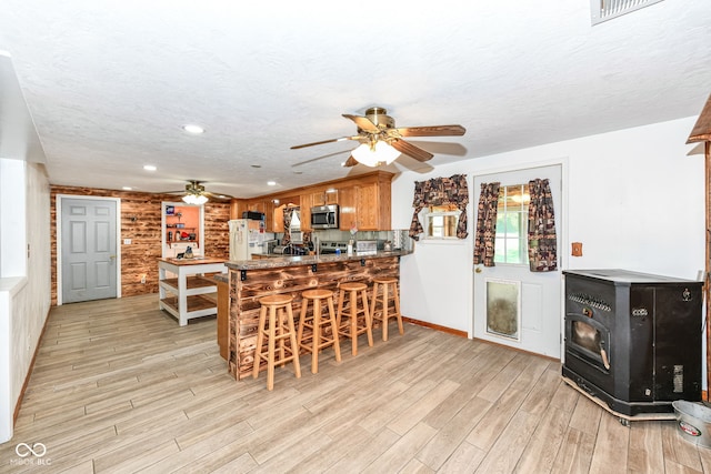 kitchen featuring a textured ceiling, light hardwood / wood-style floors, a breakfast bar area, kitchen peninsula, and appliances with stainless steel finishes