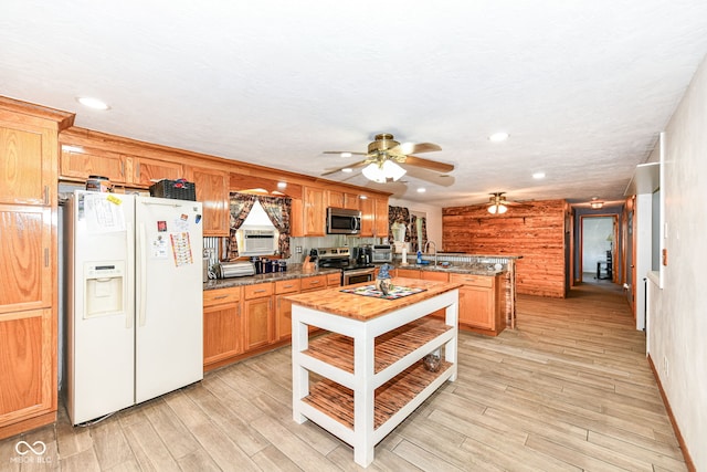 kitchen with light wood-type flooring, dark stone countertops, appliances with stainless steel finishes, and wooden walls