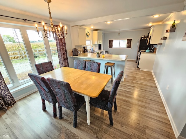 dining area featuring crown molding, a notable chandelier, sink, and light wood-type flooring