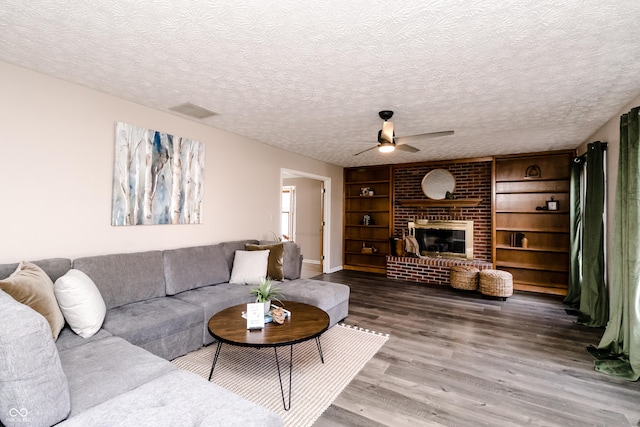 living room with built in features, ceiling fan, hardwood / wood-style floors, a fireplace, and a textured ceiling