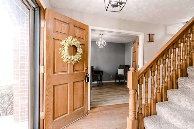 foyer featuring a notable chandelier, a textured ceiling, and light wood-type flooring