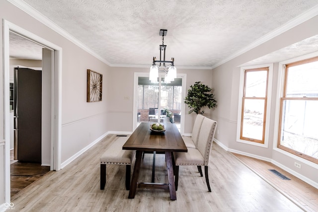 dining space featuring ornamental molding, a notable chandelier, a textured ceiling, and light hardwood / wood-style flooring