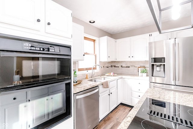 kitchen featuring tasteful backsplash, white cabinetry, sink, light stone counters, and stainless steel appliances