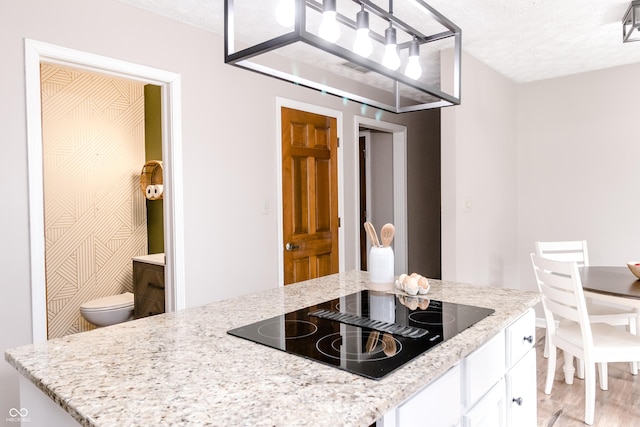 kitchen with white cabinetry, black electric stovetop, light stone countertops, and a textured ceiling