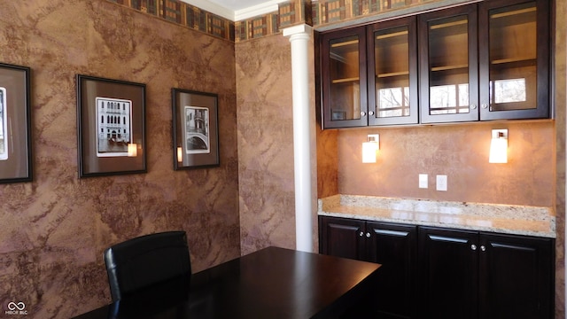 bar featuring dark brown cabinetry, decorative columns, and light stone countertops