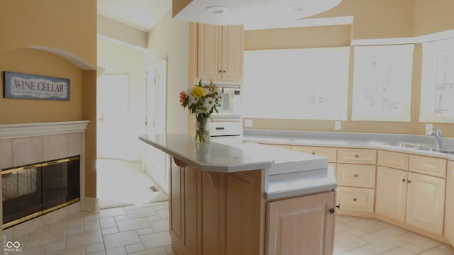 kitchen featuring a tiled fireplace, light brown cabinets, a kitchen island, and sink