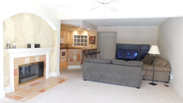 carpeted living room with ornamental molding, a tiled fireplace, and ceiling fan