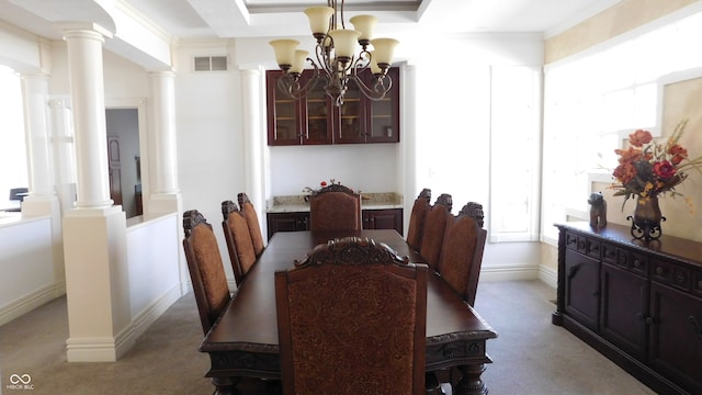 carpeted dining space featuring ornate columns, an inviting chandelier, and ornamental molding