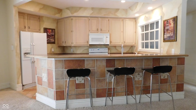 kitchen with kitchen peninsula, a kitchen bar, and white appliances