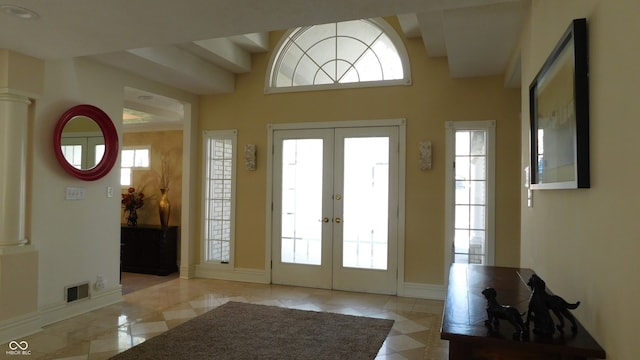 foyer entrance featuring french doors, beam ceiling, ornate columns, and a healthy amount of sunlight