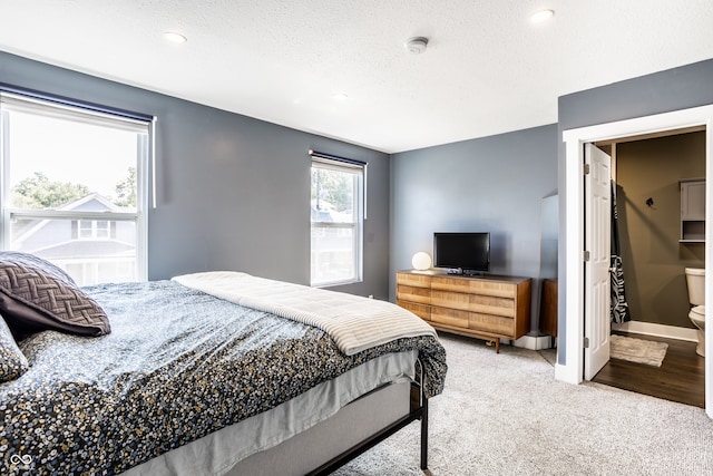 bedroom featuring light carpet, connected bathroom, and a textured ceiling