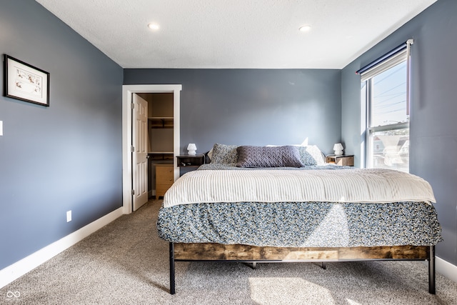 bedroom with a textured ceiling, a closet, carpet, and a walk in closet