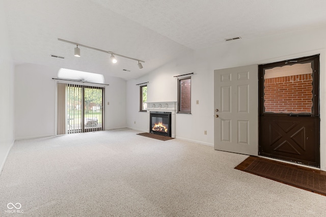 unfurnished living room featuring track lighting, carpet flooring, a textured ceiling, and vaulted ceiling