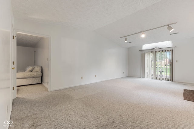 empty room with light colored carpet, a textured ceiling, lofted ceiling, and rail lighting