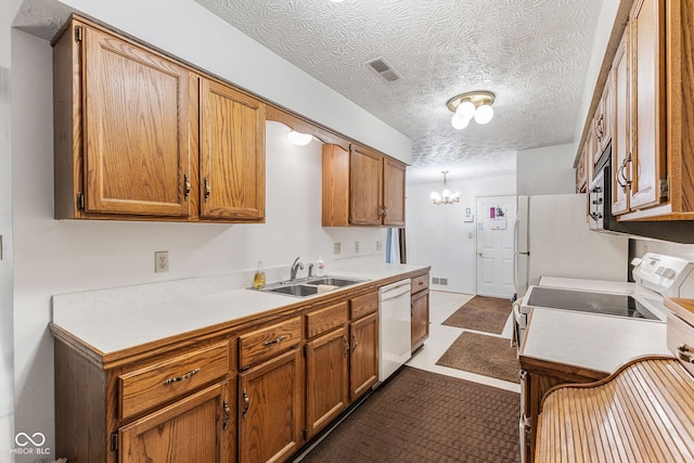 kitchen with white appliances, a textured ceiling, a chandelier, and sink