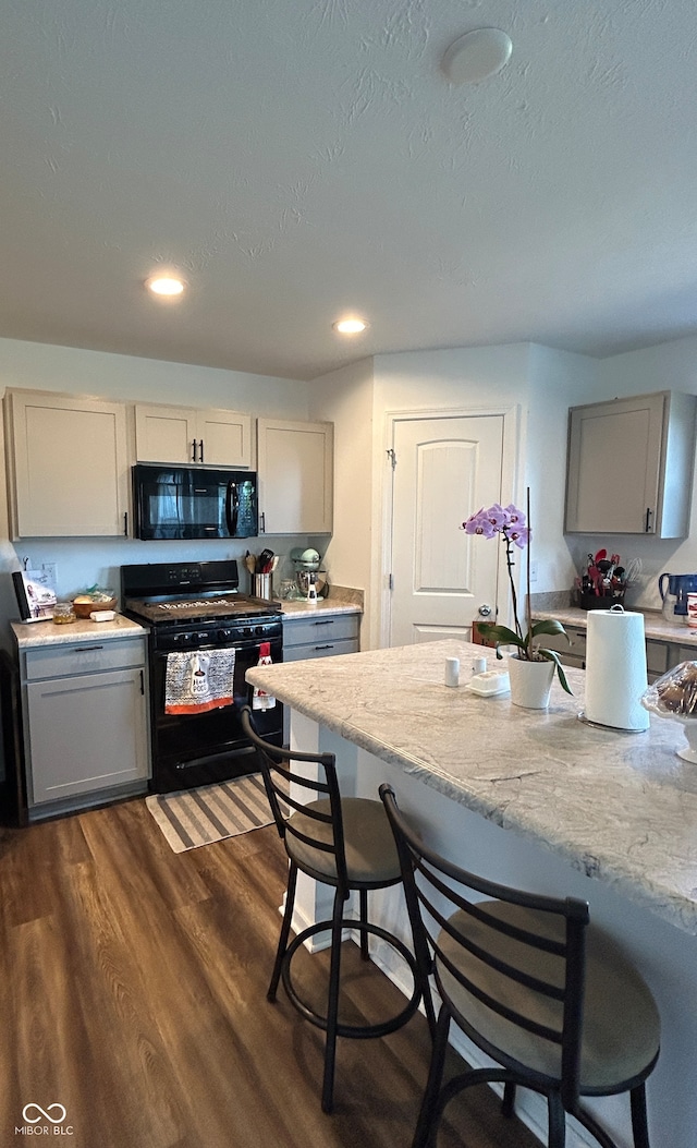 kitchen featuring black appliances, gray cabinetry, dark hardwood / wood-style floors, and a breakfast bar area