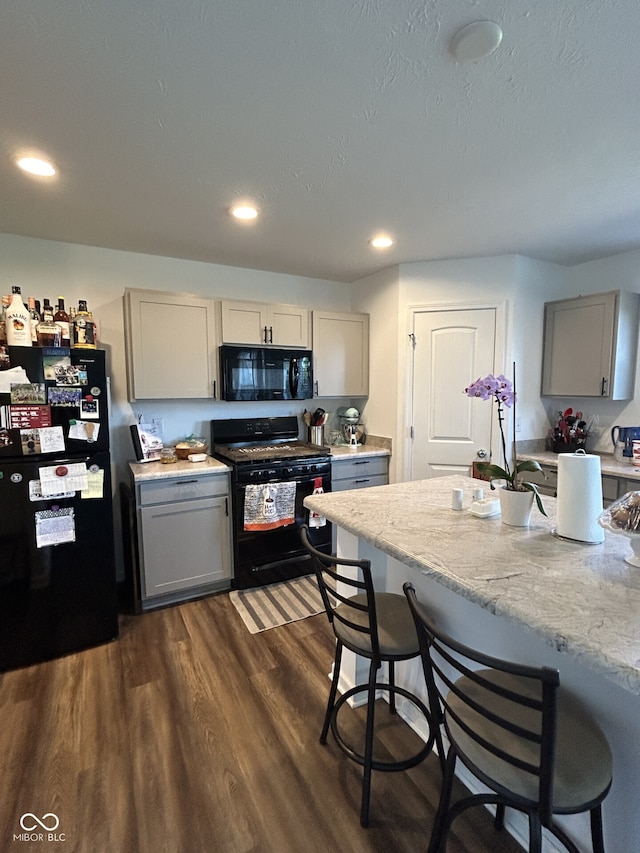 kitchen featuring gray cabinets, black appliances, dark hardwood / wood-style floors, and a breakfast bar