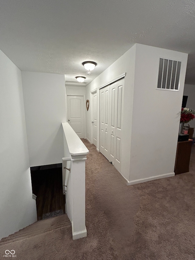 hallway featuring a textured ceiling and dark colored carpet