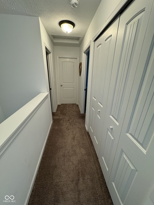 hall with dark colored carpet and a textured ceiling