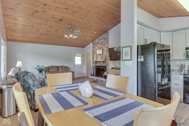 dining space with wooden ceiling, a stone fireplace, lofted ceiling, and ceiling fan