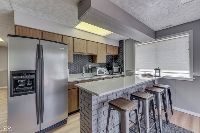 kitchen with light wood-type flooring, stainless steel refrigerator with ice dispenser, a breakfast bar area, and sink