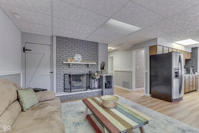 living room with light hardwood / wood-style flooring, a brick fireplace, and wood walls