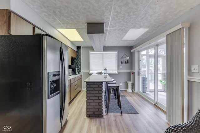 kitchen featuring a breakfast bar, backsplash, stainless steel fridge with ice dispenser, a center island, and light hardwood / wood-style floors