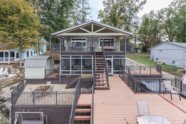 rear view of house featuring a wooden deck, a sunroom, and a storage unit