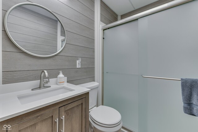 bathroom featuring wood walls, vanity, toilet, and an enclosed shower