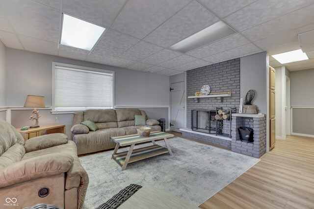 living room featuring a brick fireplace, light hardwood / wood-style floors, and a paneled ceiling