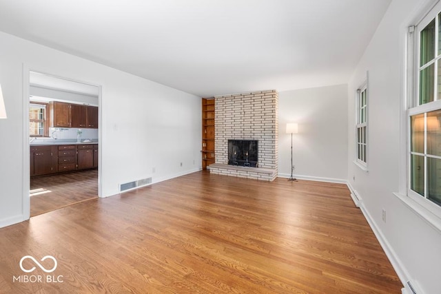 unfurnished living room featuring a brick fireplace, wood-type flooring, a baseboard heating unit, and a healthy amount of sunlight