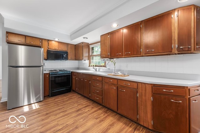 kitchen featuring black appliances, light hardwood / wood-style floors, decorative backsplash, and sink