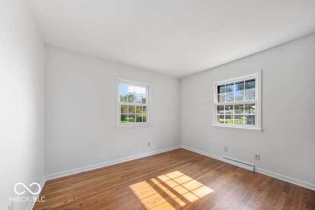 spare room with wood-type flooring, plenty of natural light, and a baseboard heating unit