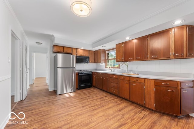 kitchen featuring stove, stainless steel refrigerator, light hardwood / wood-style flooring, decorative backsplash, and ornamental molding