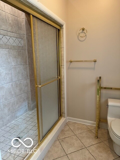 bathroom with toilet, a shower with door, and tile patterned floors