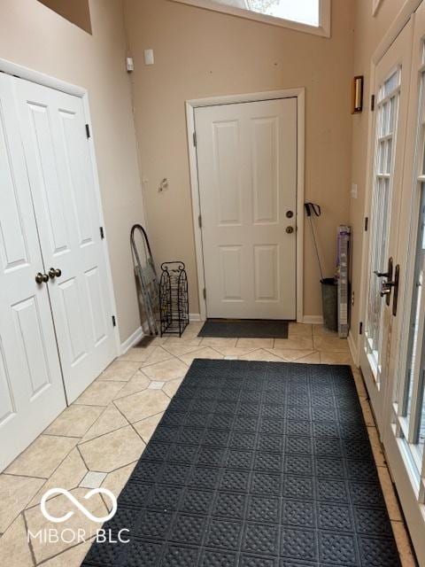 entryway featuring light tile patterned flooring, a towering ceiling, and baseboards