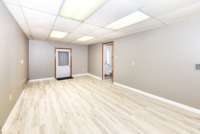 basement with a baseboard radiator, light wood-type flooring, and a drop ceiling