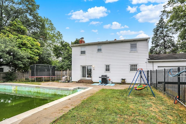 rear view of house with a trampoline, a yard, and a fenced in pool