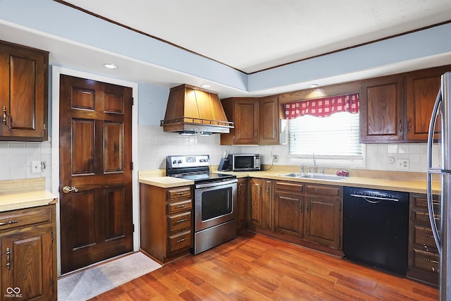 kitchen featuring premium range hood, sink, backsplash, hardwood / wood-style flooring, and stainless steel appliances