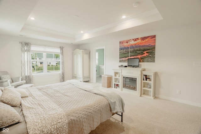 carpeted bedroom featuring a raised ceiling and connected bathroom