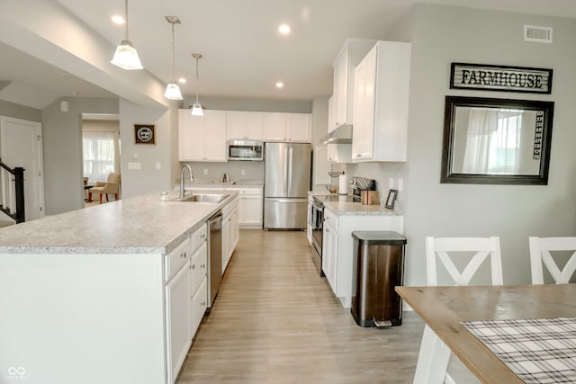 kitchen with an island with sink, sink, decorative light fixtures, white cabinetry, and appliances with stainless steel finishes