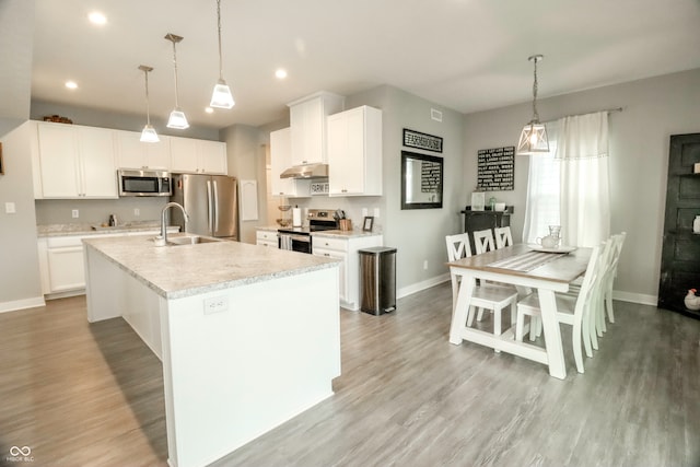 kitchen with an island with sink, stainless steel appliances, white cabinetry, and hanging light fixtures