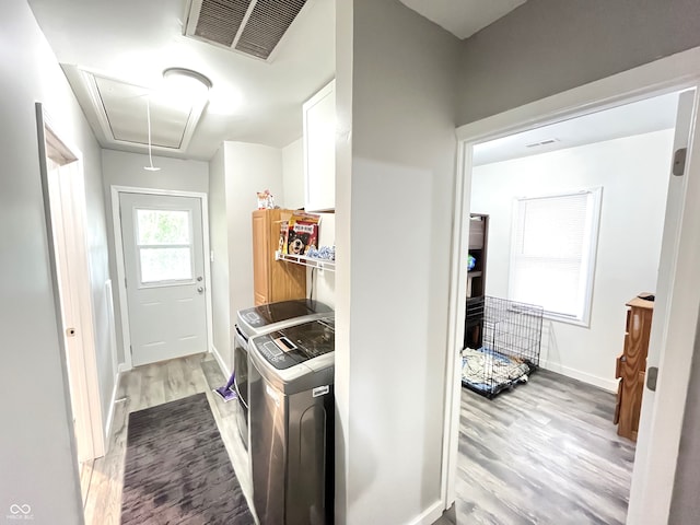 clothes washing area with cabinets, light wood-type flooring, and washer and dryer