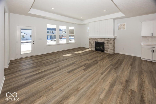 unfurnished living room featuring dark hardwood / wood-style flooring, a tray ceiling, and a stone fireplace