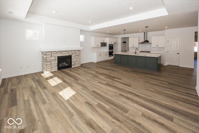 unfurnished living room with a tray ceiling, dark hardwood / wood-style flooring, sink, and a stone fireplace