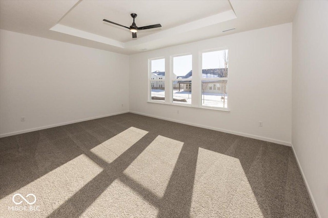 empty room with a raised ceiling, ceiling fan, and dark carpet