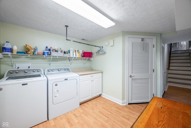 washroom with light wood-type flooring, a textured ceiling, independent washer and dryer, and cabinets