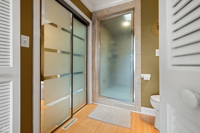 bathroom with wood-type flooring, a shower with door, toilet, and ornamental molding